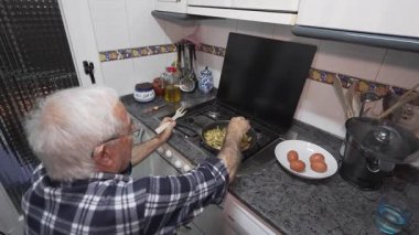 Yaşlı adam tek başına yemek pişiriyor. Yaşlı adam 80 'li yaşlarda, gömlekli.