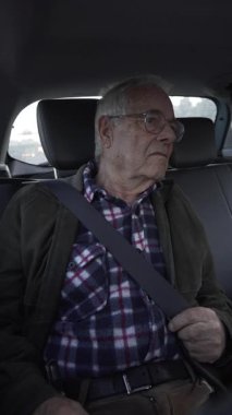 Arka koltuktaki yolcuların yatay videosu, 80 yaşını geçmiş, trafikte pencereden dışarı bakıyor ve araba kullanıyor..