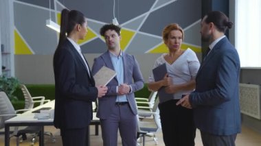 Ofisteki çalışanlar, ekip iletişim kurar, iş meselelerini tartışır. Şık ve modern ofiste takım elbiseli erkekler ve kadınlar ellerinde klasörler ve belgeler tutuyorlar..