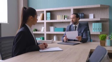 Takım elbiseli bir adam, gözlüklü bir patron, ofiste bir masada oturur, genç bir kadınla konuşur, iş meselelerini tartışır, bir kız işe girer, el sıkışır, bir kadın işe alınır..