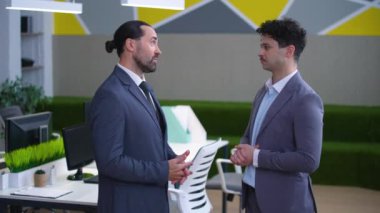 Two men, colleagues, directors in suits in the office are talking, agreeing, shaking hands, satisfied