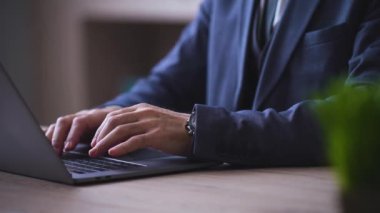 Close-up of male businessman hands typing on a modern laptop, assistant brought a cup of coffee, tea