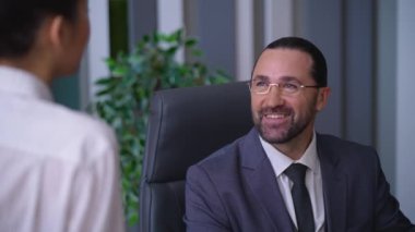 Man businessman director boss sitting in chair in office, talking with female co-worker, smiling, happy