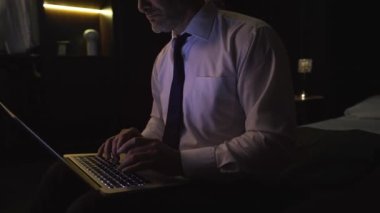 Tişörtlü ve kravatlı bir işadamı otelde elinde modern laptop, çalışıyor, daktilo ediyor, araştırma yapıyor, mektup yazıyor.