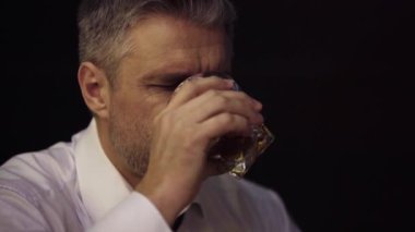 Yakın planda, bir adamın portresi, bir iş adamı bardaktan alkol içer, iç çeker, yorulur, gözlerini kapatır.