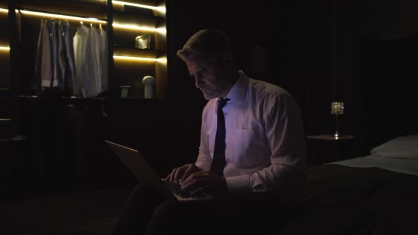 一个穿衬衫打领带的男人 一个商人 坐在旅馆的床上 拿着一台现代笔记本电脑 做研究 — 图库视频影像
