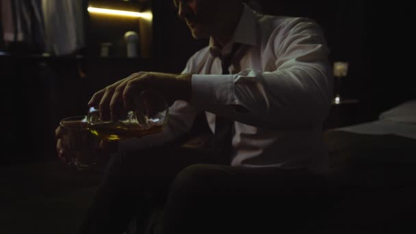 スーツを着た男がホテルの自宅のベッドに座り アルコールを1本持ってガラスに注ぐ ビジネスマンは ウイスキー スコッチ コニャックを飲み 厳しい一日の後にリラックスし ビジネスミーティング — ストック動画