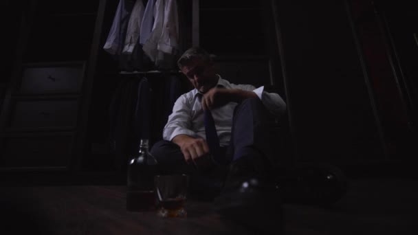 一位穿着白衬衫打领带的商人坐在地板上一家宾馆的房间里 手里拿着一杯酒 喝着苏格兰威士忌 这个人很疲倦 很不高兴 很难过 收到了坏消息 — 图库视频影像