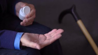 Yaşlı bir adamın elinde yakın plan bir fotoğraf, büyükbaba paketten avucunun içine bir hap döker. Avuç içlerine iki hap yakın plan.