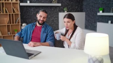 Genç adam ve kadın iş arkadaşları laptopun önünde oturmuş ofiste duygusal olarak mutsuz konuşuyorlar.