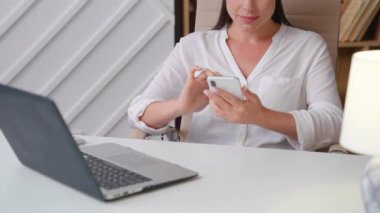 Evde, masada oturan genç bir kadın telefonu elinde tutuyor. Haberler gülümsüyor. Yakın plan.