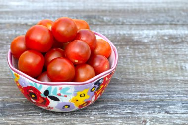 Red cherry tomatoes in the bright floral bowl on the wooden table.