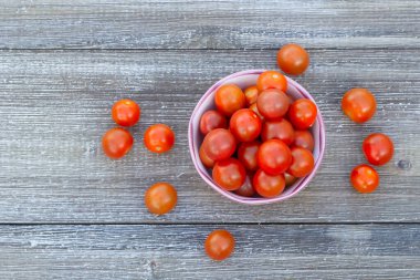 Top view of red cherry tomatoes in the bright floral bowl on the wooden table.