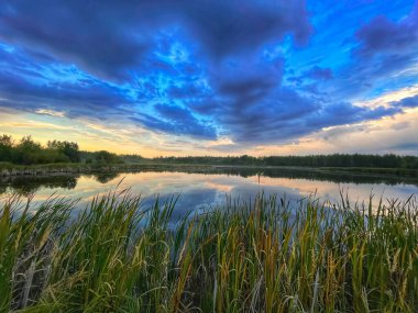 Scenic sunset over the lake in a provincial park. Blue cloudy dramatic sky and reflection on the water.