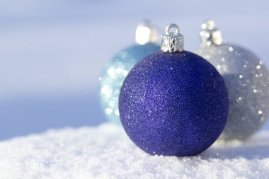 Geleneksel mavi ve gümüşi yeni yıl süsleme kürelerini beyaz kar ve mavi arkaplanla kapatın.