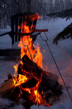 Kamp alanındaki ateşin yanında kış pikniği sosisleri parktaki çubuklarda şöminenin üstünde kızarıyor..