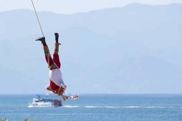 Mexican dance of the flyer, volador is hanging on the cable from the pole and performing the ancient ritual. Sea and mountains on the background.