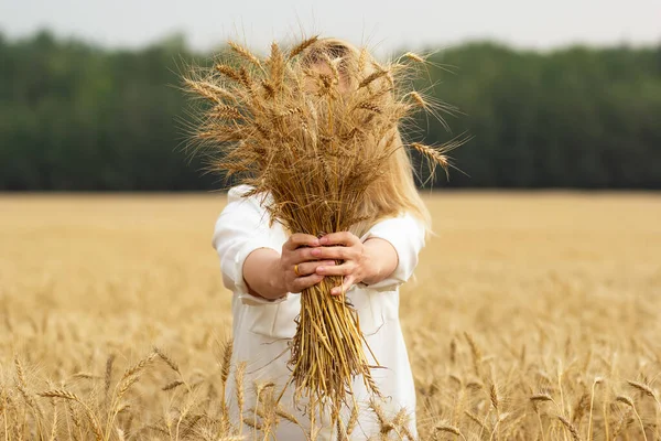 在金色的农田里 女农手里拿着一大捆麦穗 后面是森林 — 图库照片
