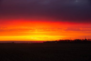 Otoyol boyunca turuncu ve mor ışıkla parlak güzel bir gün doğumu ve sonbaharda ufuk çizgisindeki çiftlikteki tahıl kutularının siluetleri..