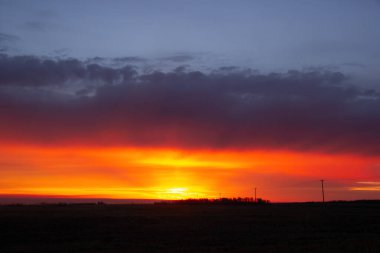 Otoyol boyunca turuncu ve mor ışıkla parlak güzel bir gün doğumu ve sonbaharda ufuk çizgisindeki çiftlikteki tahıl kutularının siluetleri..