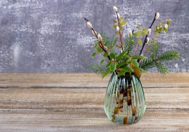 Easter bouquet from the wood - branches of pussy willow, labrador tea, fir, bear berry in a little vase on the wooden brown table.