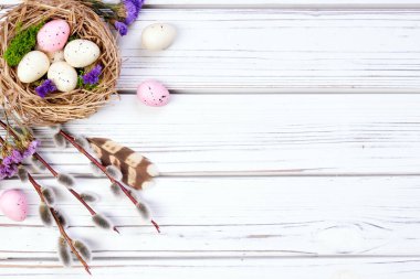 Düz Paskalya kompozisyonu bir yuva ve yumurta, söğüt dalları, stativ çiçekleri, beyaz ahşap arka planda tüyler.