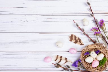 Düz Paskalya kompozisyonu bir yuva ve yumurta, söğüt dalları, stativ çiçekleri, beyaz ahşap arka planda tüyler.