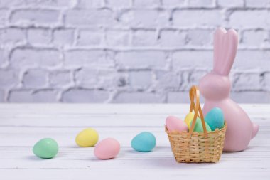 Minimum Paskalya kompozisyonu, pembe bir tavşan heykeli ve renkli yumurta şekilli şekerlerle dolu küçük bir hasır sepet..