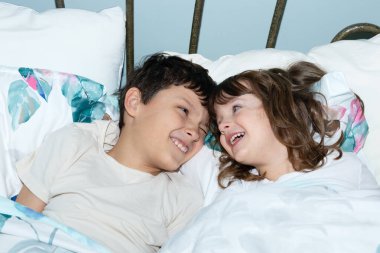Ergen erkek ve küçük kız kardeş sabahları yatakta yatarken birbirlerine gülümsemekten mutlu olurlar. Yeşil yapraklı beyaz yatak.