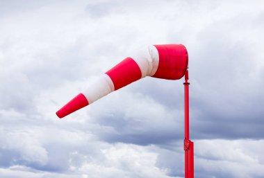 Çizgili kırmızı ve beyaz rüzgar gülü fırtınadan önce arka planda koyu mavi bulutlu gökyüzü ile rüzgarda uçar..