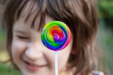 Renkli yuvarlak spiral lolipopun yakın çekimi ve arka planda suratını buruşturan bir kızın yüzü..