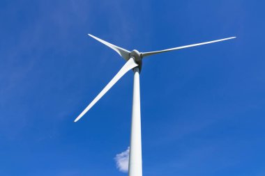 Doğal kaynaklardan sürdürülebilir enerji üreten dev bir rüzgar türbini. Arka planda küçük bir bulut olan mavi gökyüzü..
