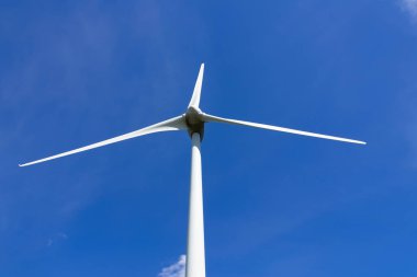 Doğal kaynaklardan sürdürülebilir enerji üreten dev bir rüzgar türbini. Arka planda küçük bir bulut olan mavi gökyüzü..
