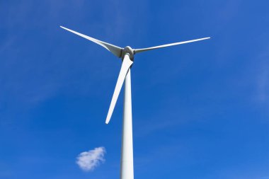 Doğal kaynaklardan sürdürülebilir enerji üreten dev bir rüzgar türbini. Arka planda küçük bir bulut olan mavi gökyüzü..