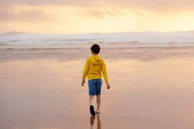 Genç çocuk yalnızlığın tadını çıkarıyor ve gün batımında huzurlu plajda yürüyor. Tofino, Vancouver Adası, Kanada.