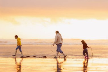 Baba, gün batımında turuncu ışıkta koşan ve yosun yosunlarıyla oynayan iki çocuk. Tofino, Vancouver Adası, Kanada.