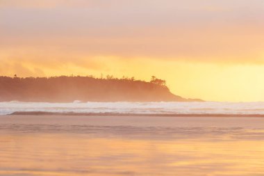 Güzel bir akşam manzarası, Pasifik Okyanusu 'nda gün batımı kaya ve ağaçlardan oluşan siluetler, turuncu güneş ışığı ve suda dalgalar. Tofino, Vancouver Adası, Kanada.