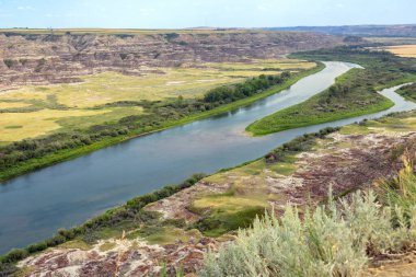 Çorak topraklar boyunca uzanan vadideki tepeden nehre kadar uzanan harika bir yaz manzarası. Kızıl Geyik Nehri, Orkney Gözcüsü, Alberta, Kanada.