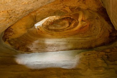 Beauty exploration inside a yellow cave with wonderful pattern, spiral ceiling with a light beam from the eroded hole. Gundy caves, British Columbia, Canada. clipart