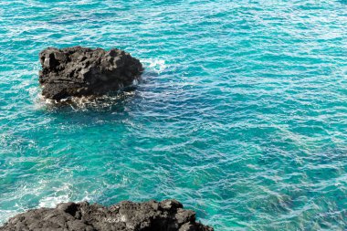 Pasifik Okyanusu 'nun turkuaz sularında oluşan siyah volkanik kayalar. Büyük Ada, Hawaii, ABD.