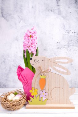 Tahta oymalı tavşanlı güzel Paskalya dekoru, beyaz ahşap masa üzerinde çiçek açan pembe sümbülü saksı..