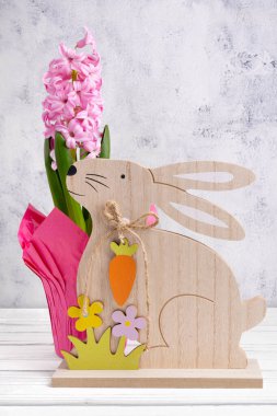 Tahta oymalı tavşanlı güzel Paskalya dekoru, beyaz ahşap masa üzerinde çiçek açan pembe sümbülü saksı..
