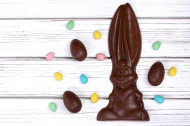 Paskalya dekorunun düz yatışı ahşap bir kırsal masa üzerinde büyük bir çikolata tavşanı ve çeşitli tatlı yumurtalarla.