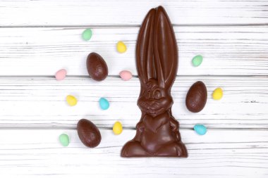 Paskalya dekorunun düz yatışı ahşap bir kırsal masa üzerinde büyük bir çikolata tavşanı ve çeşitli tatlı yumurtalarla.