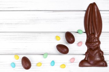 Paskalya dekorunun düz yatışı ahşap bir kırsal masa üzerinde büyük bir çikolata tavşanı ve çeşitli tatlı yumurtalarla.