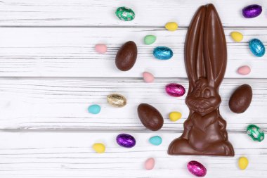 Paskalya dekorunun düz yatışı ahşap bir kırsal masa üzerinde büyük bir çikolata tavşanı ve çeşitli tatlı yumurtalarla.