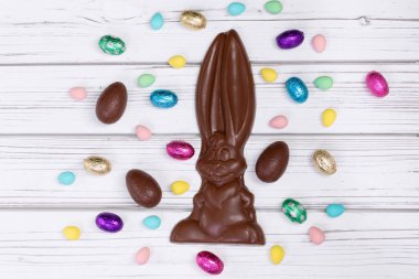 Paskalya dekorunun düz yatışı ahşap bir kırsal masa üzerinde büyük bir çikolata tavşanı ve çeşitli tatlı yumurtalarla.