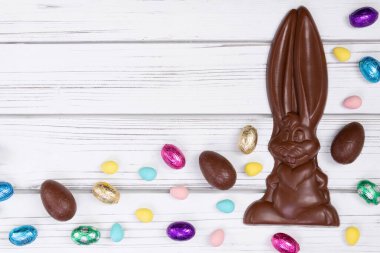 Paskalya dekorunun düz yatışı ahşap bir kırsal masa üzerinde büyük bir çikolata tavşanı ve çeşitli tatlı yumurtalarla.