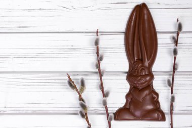 Flat lay of Easter decor on a wooden rustic white table with chocolate big bunny and branches of pussy willow.