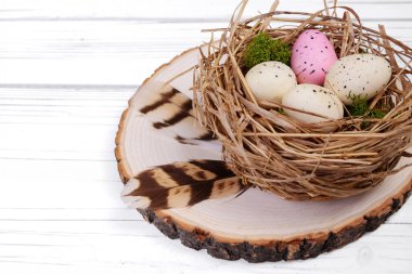 Paskalya deseni - benekli pembe ve bej renkli küçük yumurtalarla saman yuvası ve ahşap yuvarlak yeşil yosun etrafında kahverengi tüyler olan ahşap ahşap bir masa üzerinde.